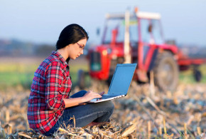 ragazza seduta su campo con pc portatile e sfondo di un trattore
